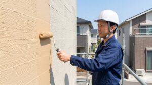 積水ハウスのダインコンクリート外壁を象徴する、複雑で凹凸のある壁面を、ローラーを使って丁寧に塗装する日本人の塗装職人。明るい太陽光の下で作業が進行している。