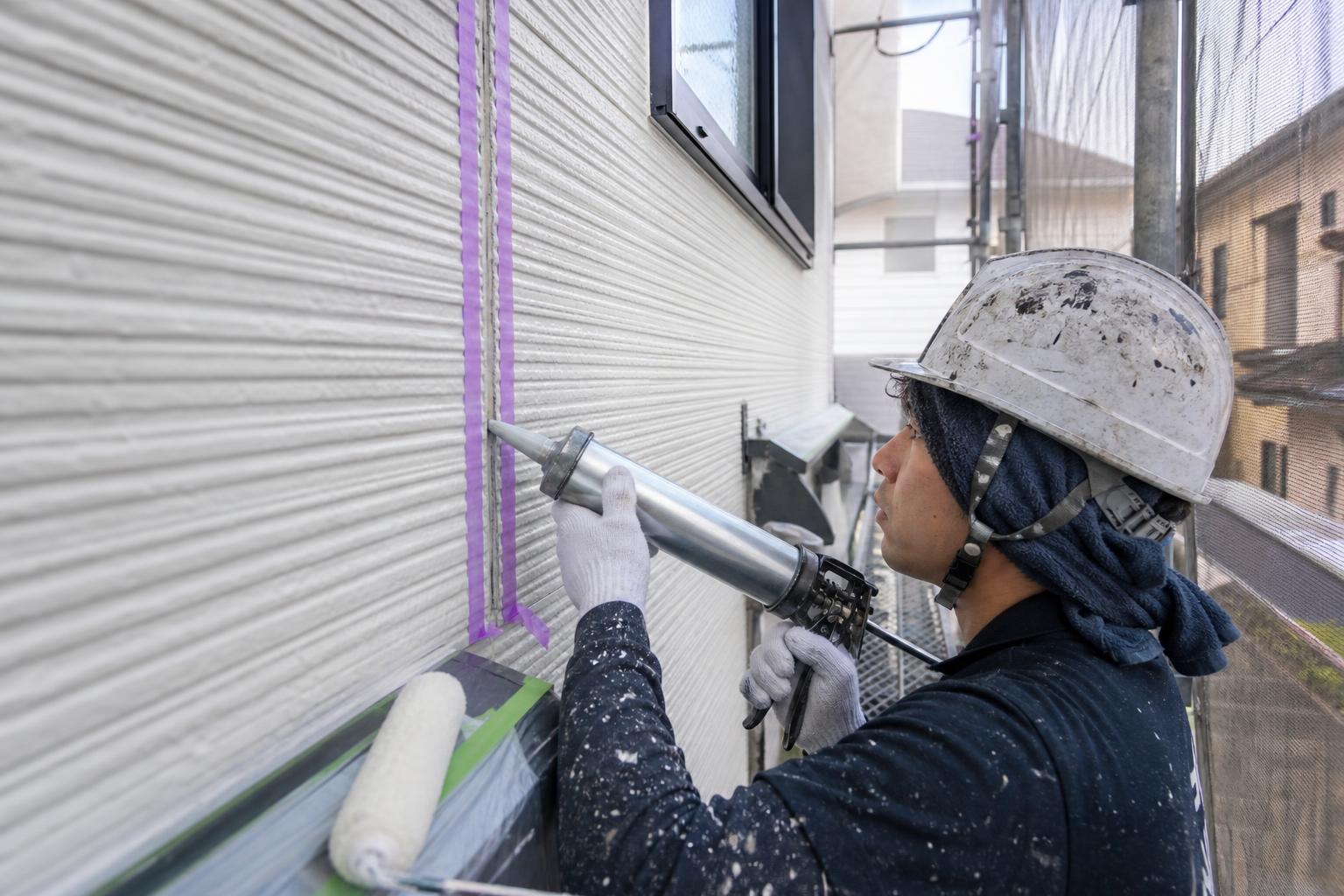 足場を設置した戸建てでコーキングを打ち替える職人
